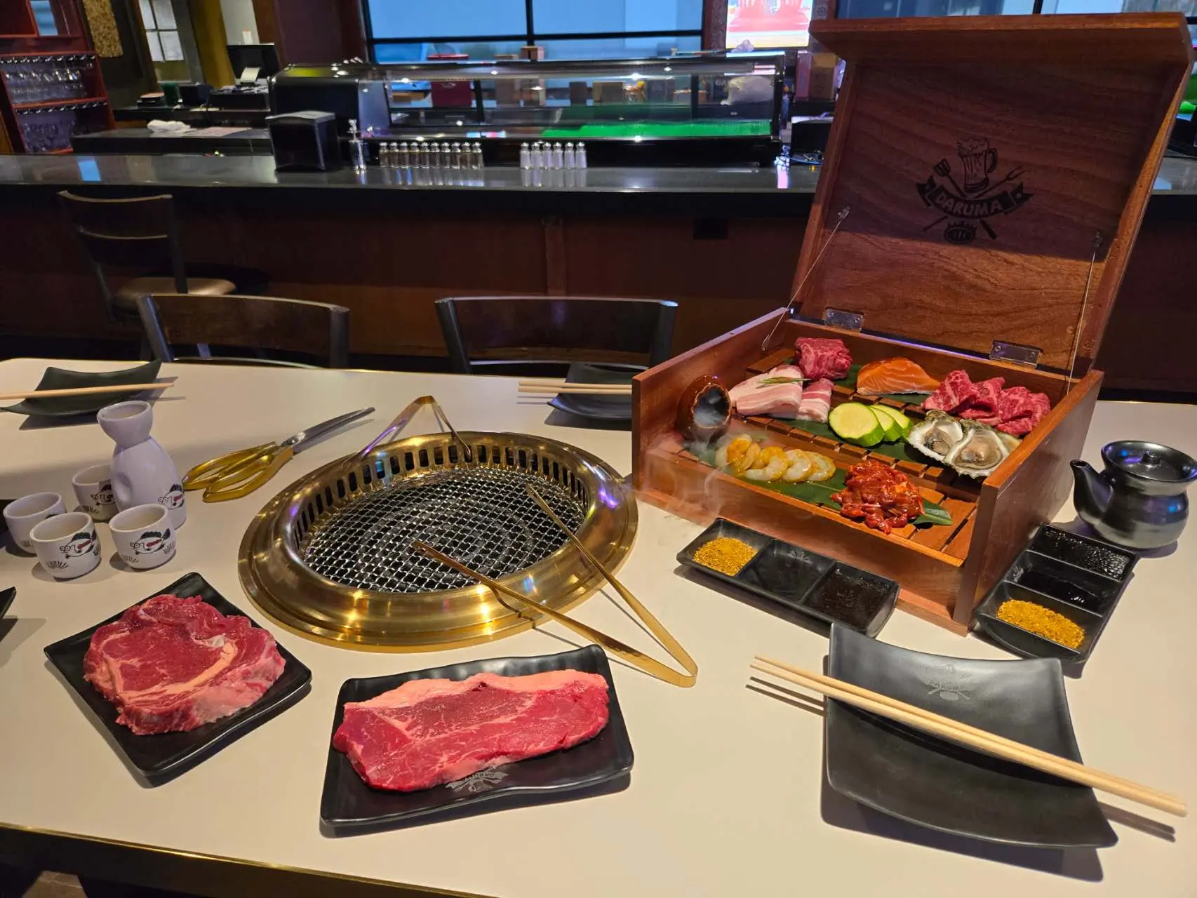 BBQ dining setup with grill, assorted meats, sauces, and a wooden box platter at Daruma BBQ & Sushi AYCE, a Asian Restaurant in Holyoke
