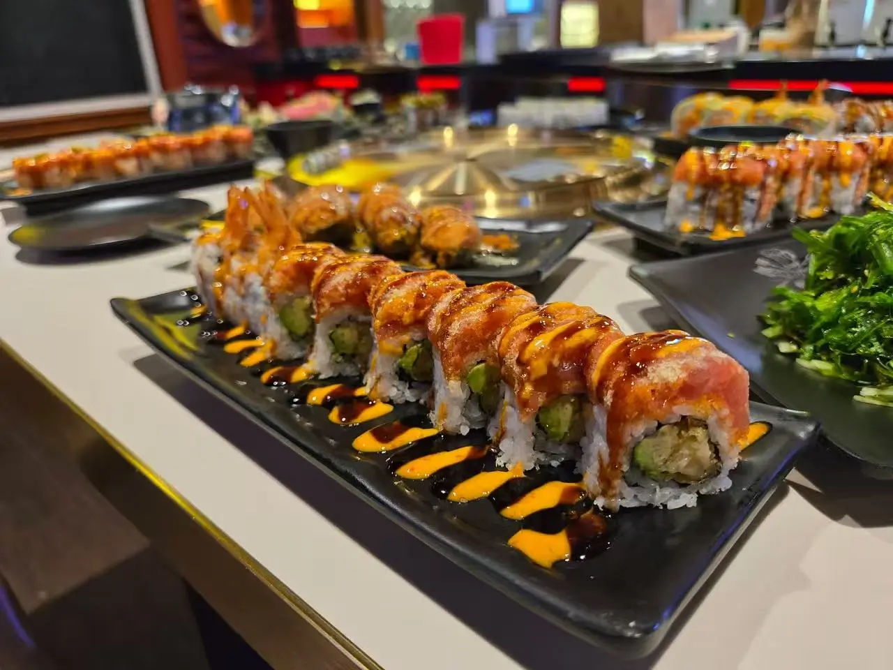 Tuna avocado sushi roll drizzled with dual sauces, served on a black platter at Daruma BBQ & Sushi AYCE, a Asian Restaurant in Holyoke